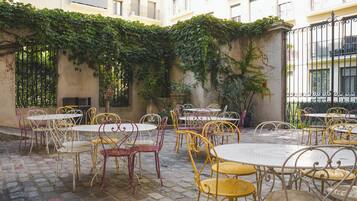 Un patio al aire libre con mesas y sillas, rodeado de un suelo de piedra y una pared cubierta de plantas trepadoras.