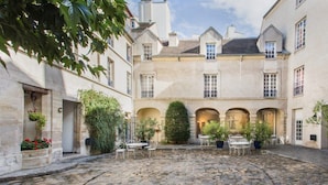 A courtyard with stone flooring, potted plants, and outdoor seating. - MIJE Marais - Hostel (Paris)