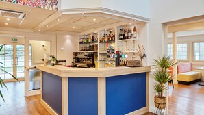 Un espace bar avec un mur d’accent bleu, des étagères remplies de différentes bouteilles et un coin salon agrémenté d’une plante.