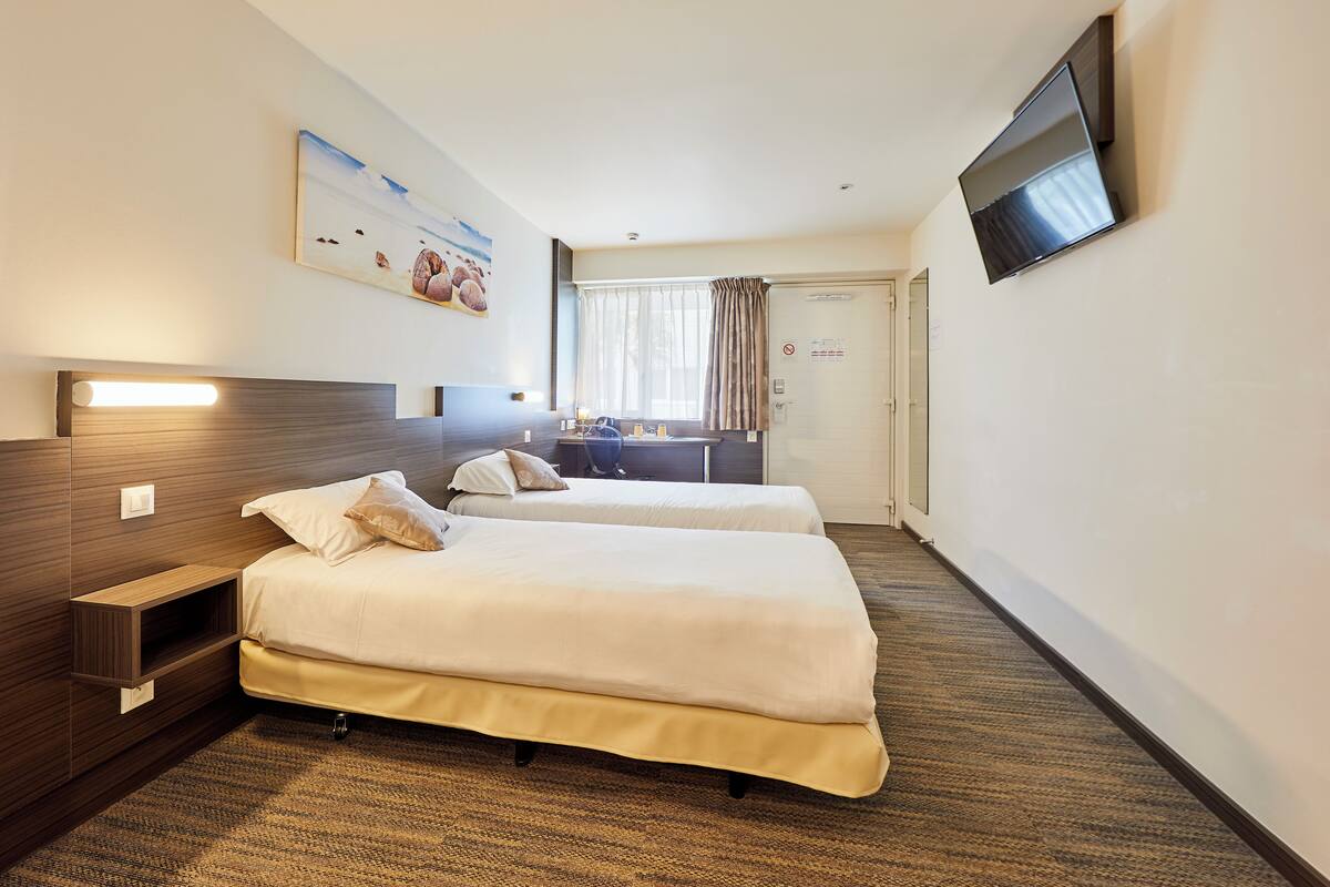 A hotel room with two beds, a desk, a flat-screen TV, and a painting on the wall.