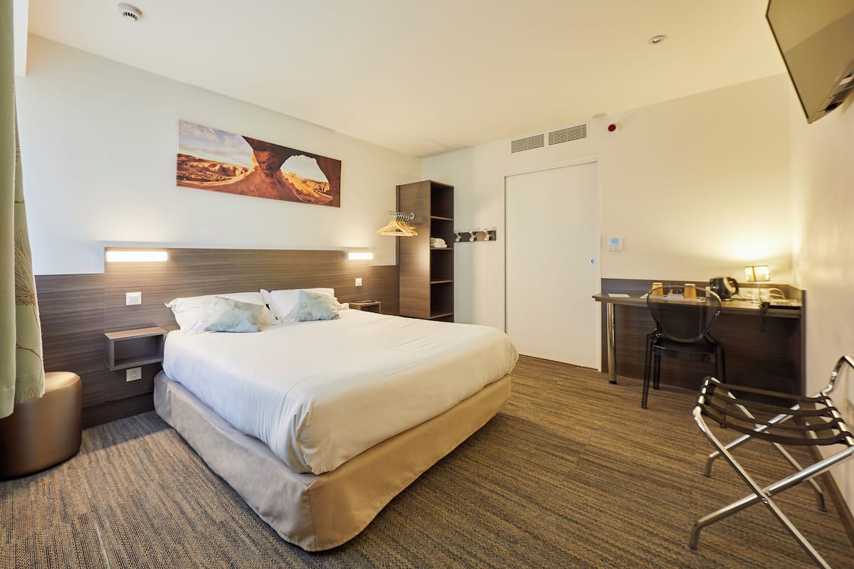 A hotel room with a large bed, a desk, and a chair.