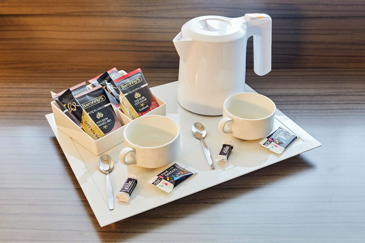 A tray with a white coffee pot, two white cups, a spoon, and several packets of Barony's tea.