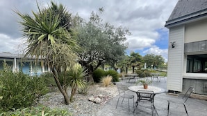 Une terrasse avec une table ronde et des chaises, entourée de différentes plantes et arbres.