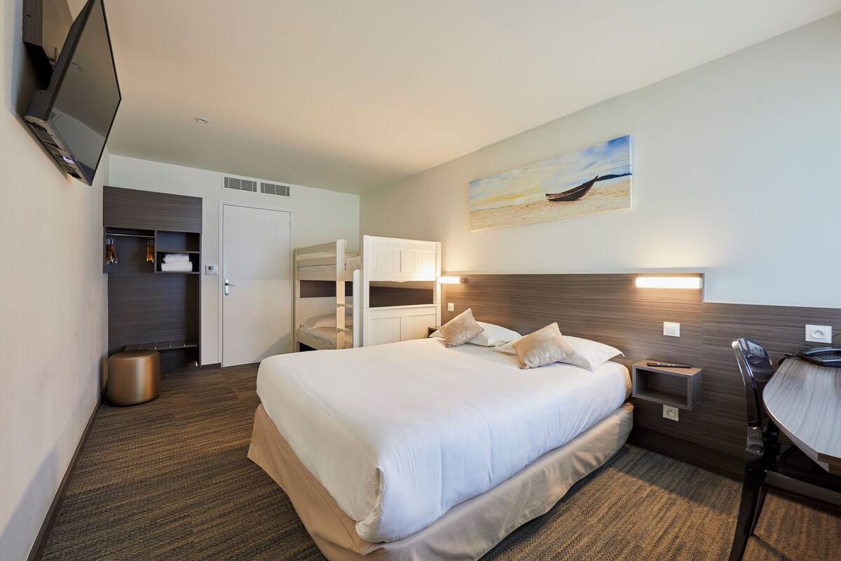 A hotel room with a large bed, a desk with a chair, a TV mounted on the wall, and a painting above the bed.