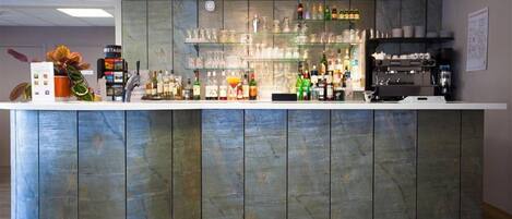 Una zona de bar con una barra curva, estantes con botellas y una máquina de café.