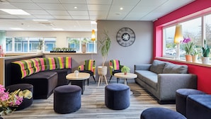 Un espace de détente moderne, avec des canapés, des poufs et une grande horloge murale.
