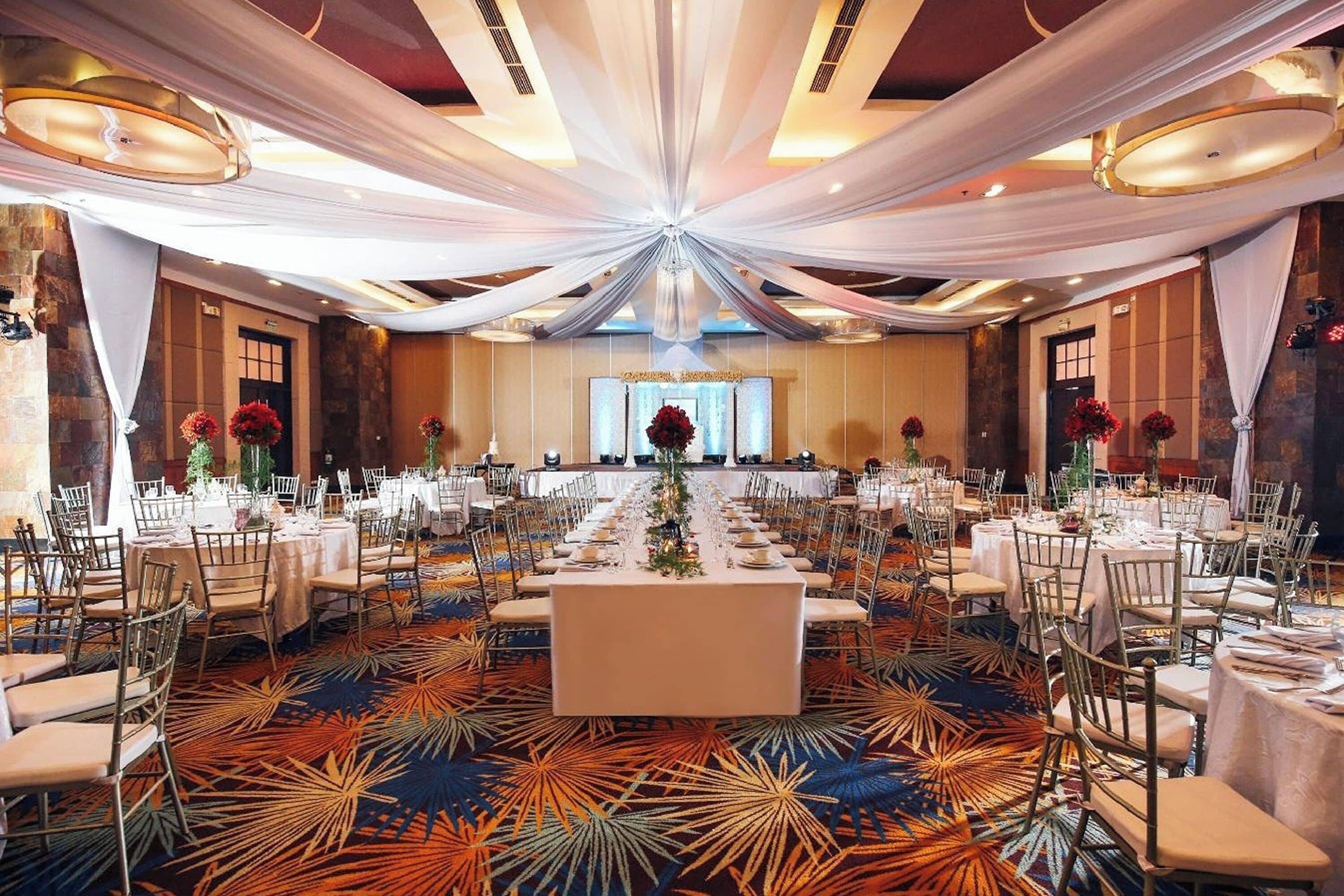 A banquet hall with tables set for a formal event, featuring a central aisle and draped ceiling decorations.