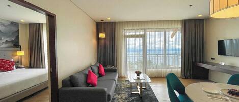 A hotel room with a bed, a sofa, a dining table, and a TV.