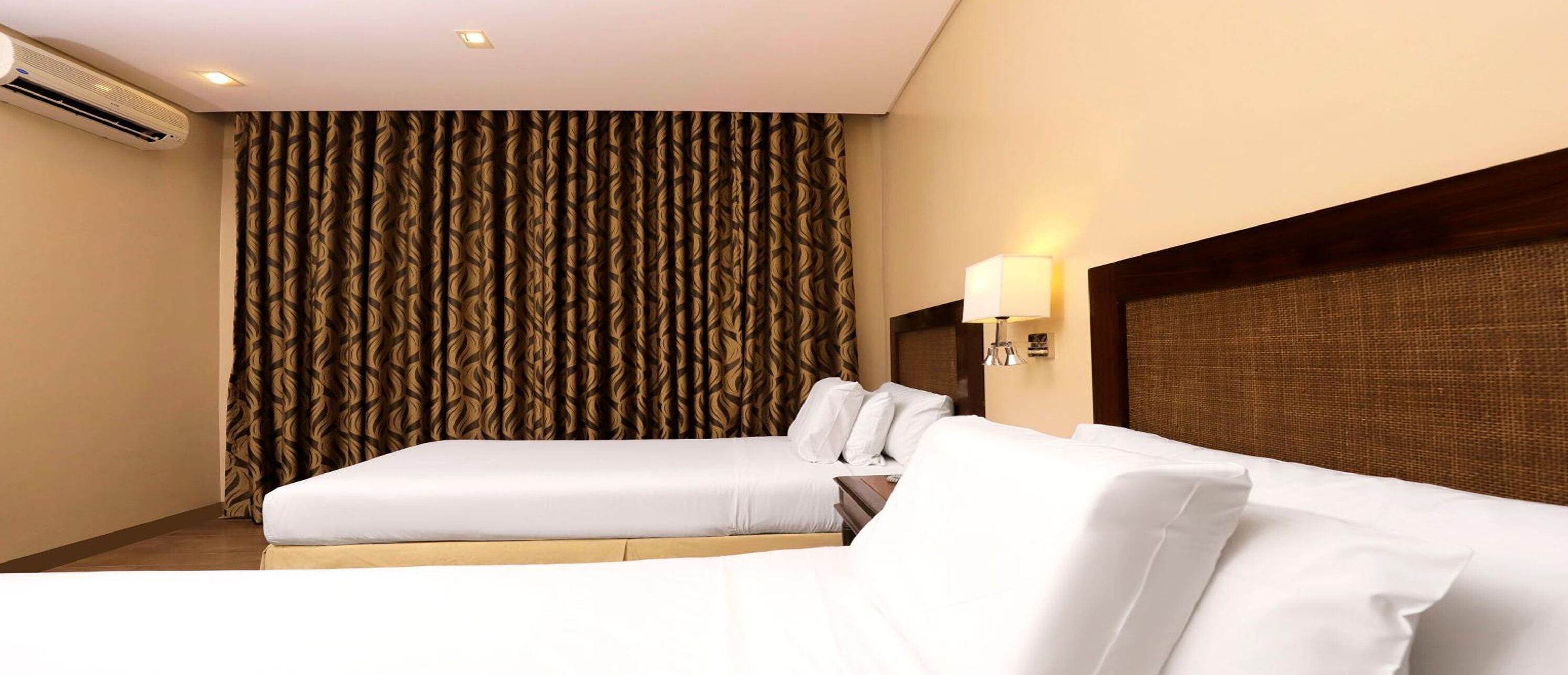 Una habitación de hotel con una cama, una mesita de noche, una lámpara y una cortina estampada.