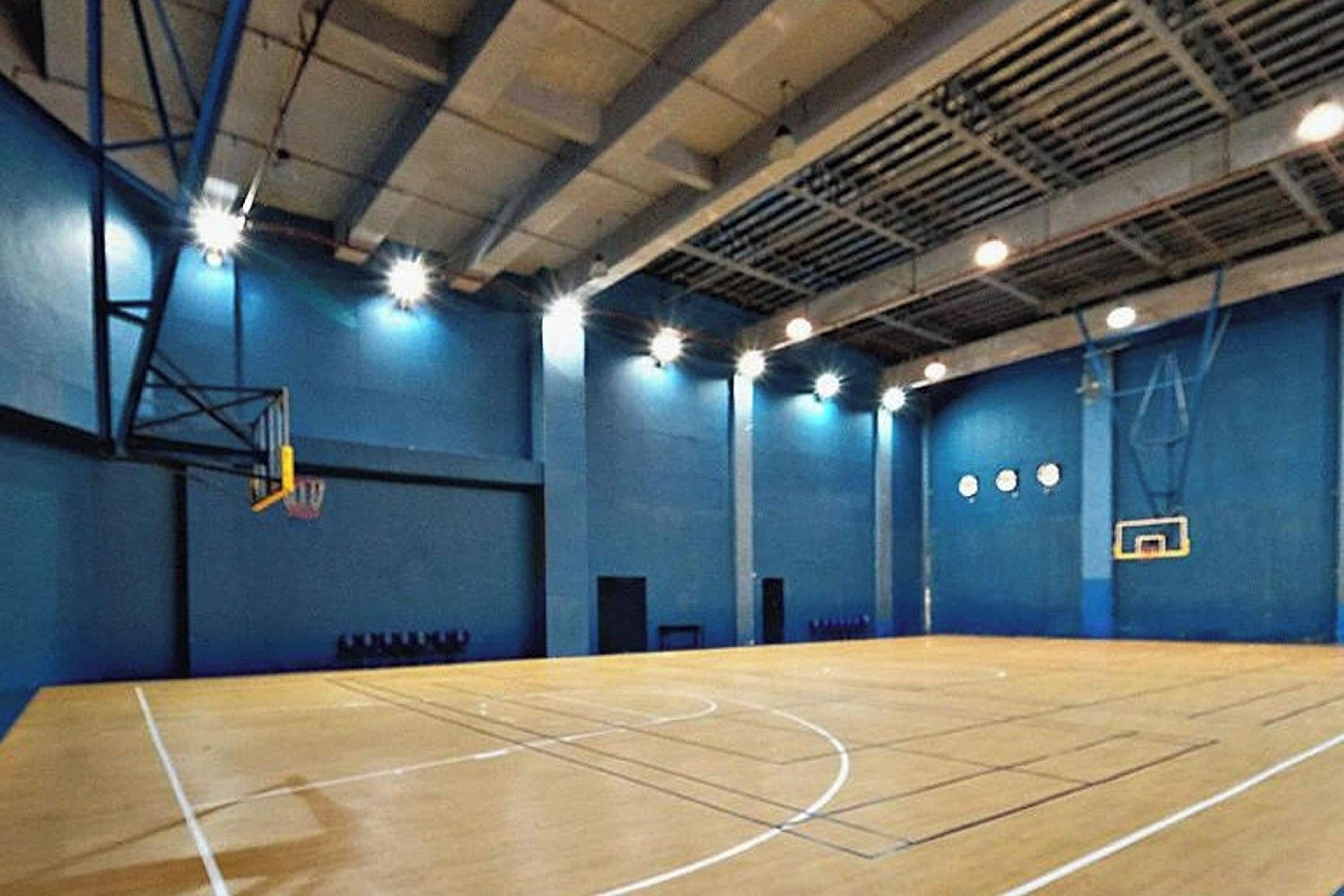 An indoor basketball court with a wooden floor, blue walls, and multiple basketball hoops.