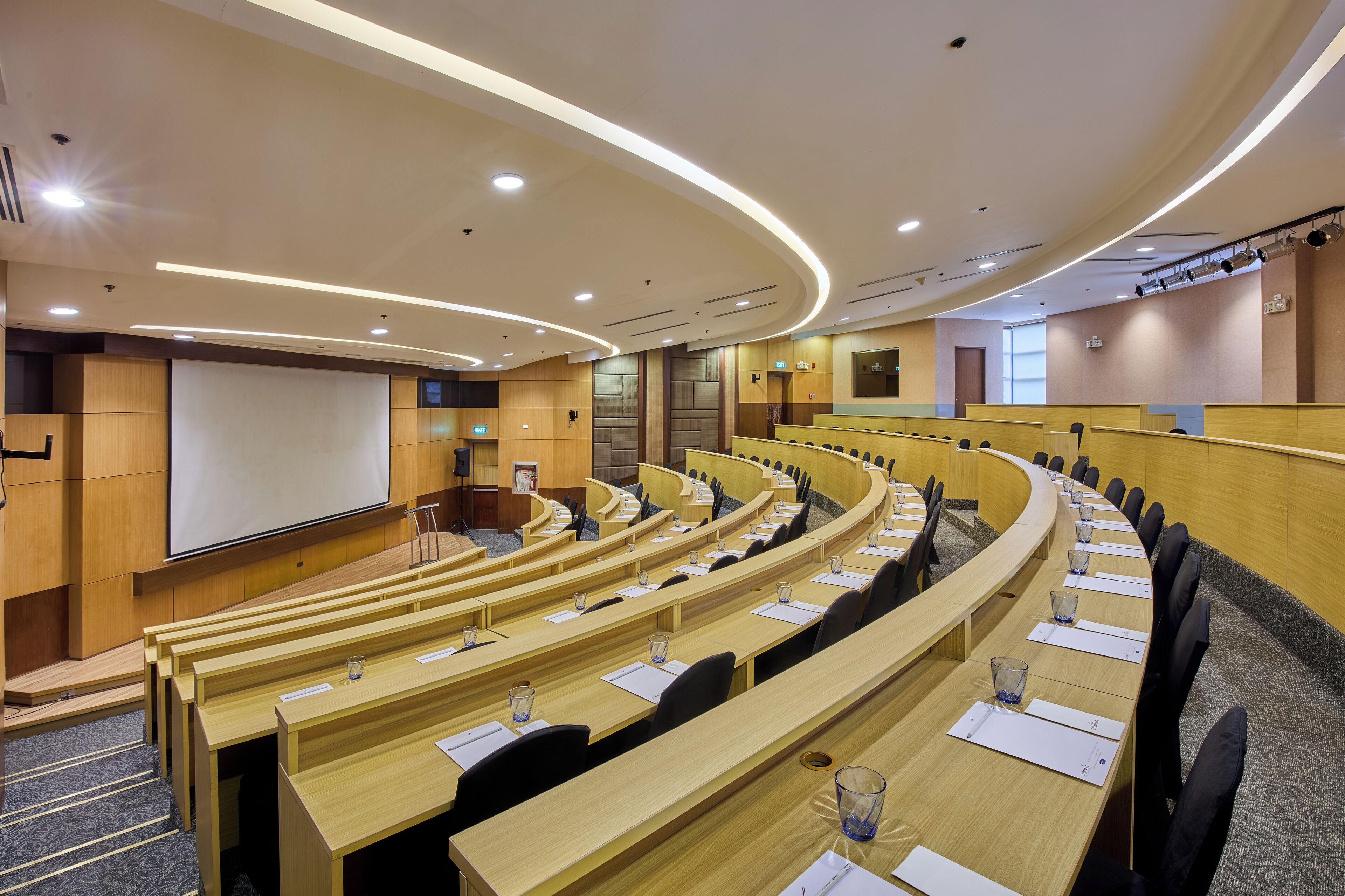 Une salle de conférence dotée de sièges en gradins, d’un écran de projection et d’une scène.