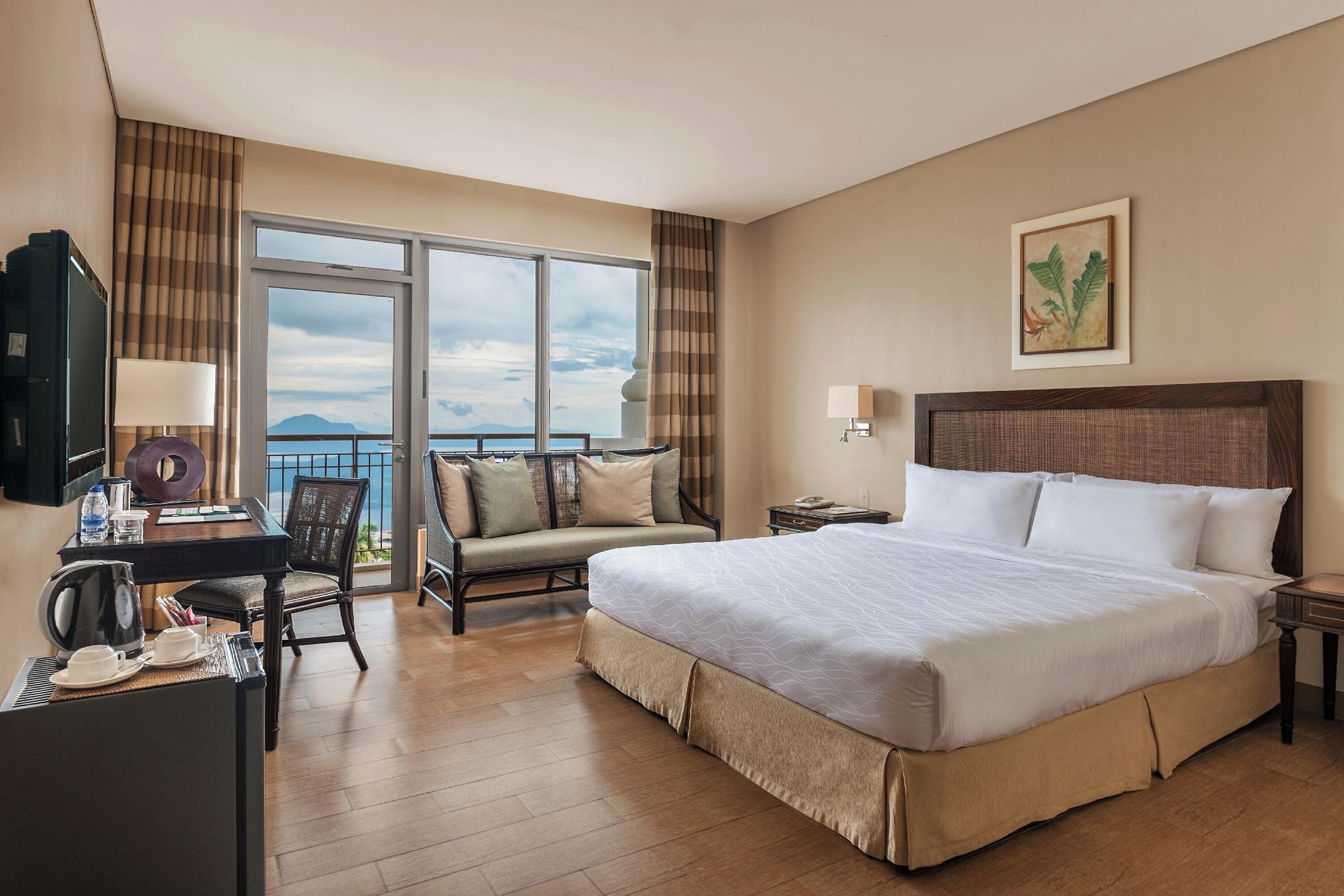Ein Hotelzimmer mit einem großen Bett, einem Schreibtisch mit Stuhl, einer Couch und einem Balkon mit Aussicht.