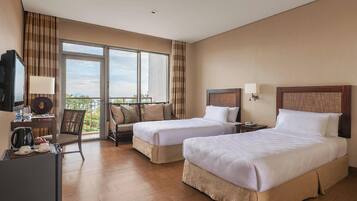 A hotel room with two beds, a desk with a television, a chair, and a balcony with a view.
