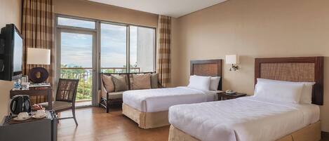 A hotel room with two beds, a desk with a television, a chair, and a balcony with a view.