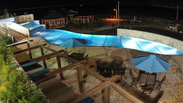 Zona de piscina en la azotea con barandilla de cristal, mobiliario exterior y vistas de los edificios circundantes.