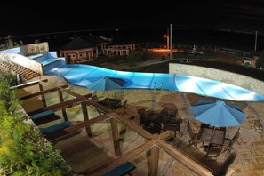 A rooftop pool area with a glass balustrade, outdoor seating, and a view of the surrounding buildings.