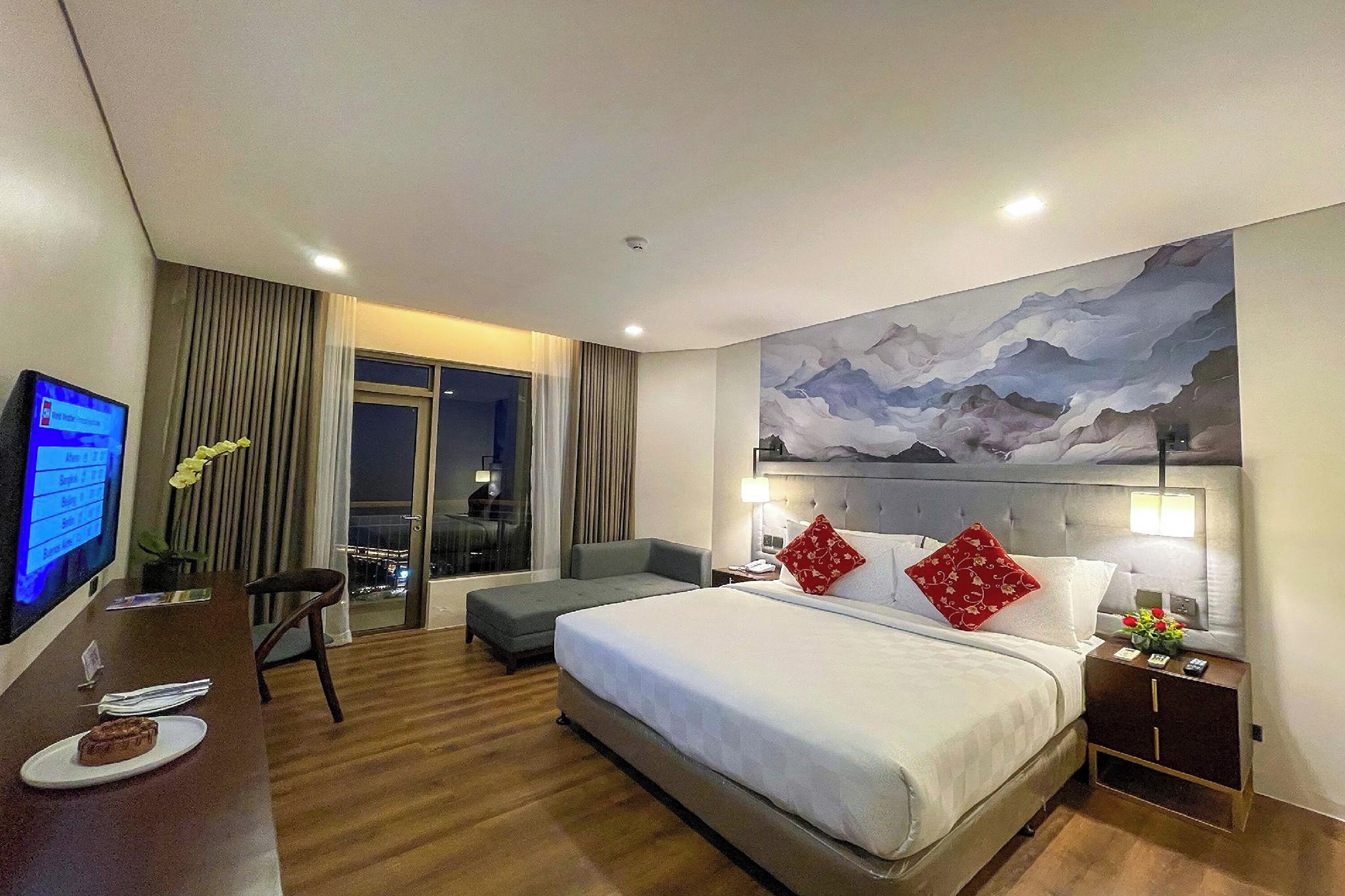 A hotel room with a bed, a desk, a chair, and a large window.