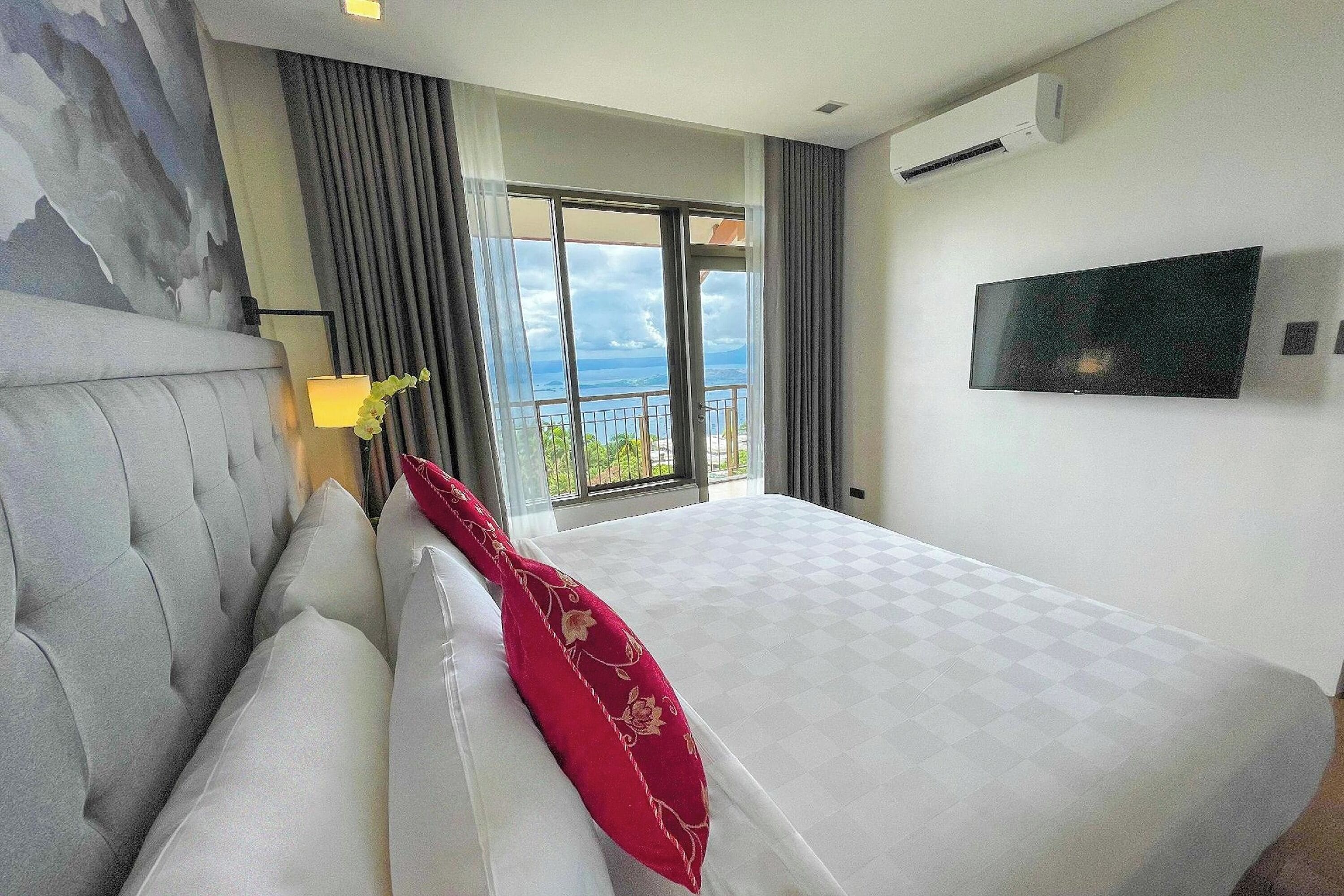 Een hotelkamer met een groot bed, een aan de muur bevestigde televisie en een balkon met uitzicht op zee.