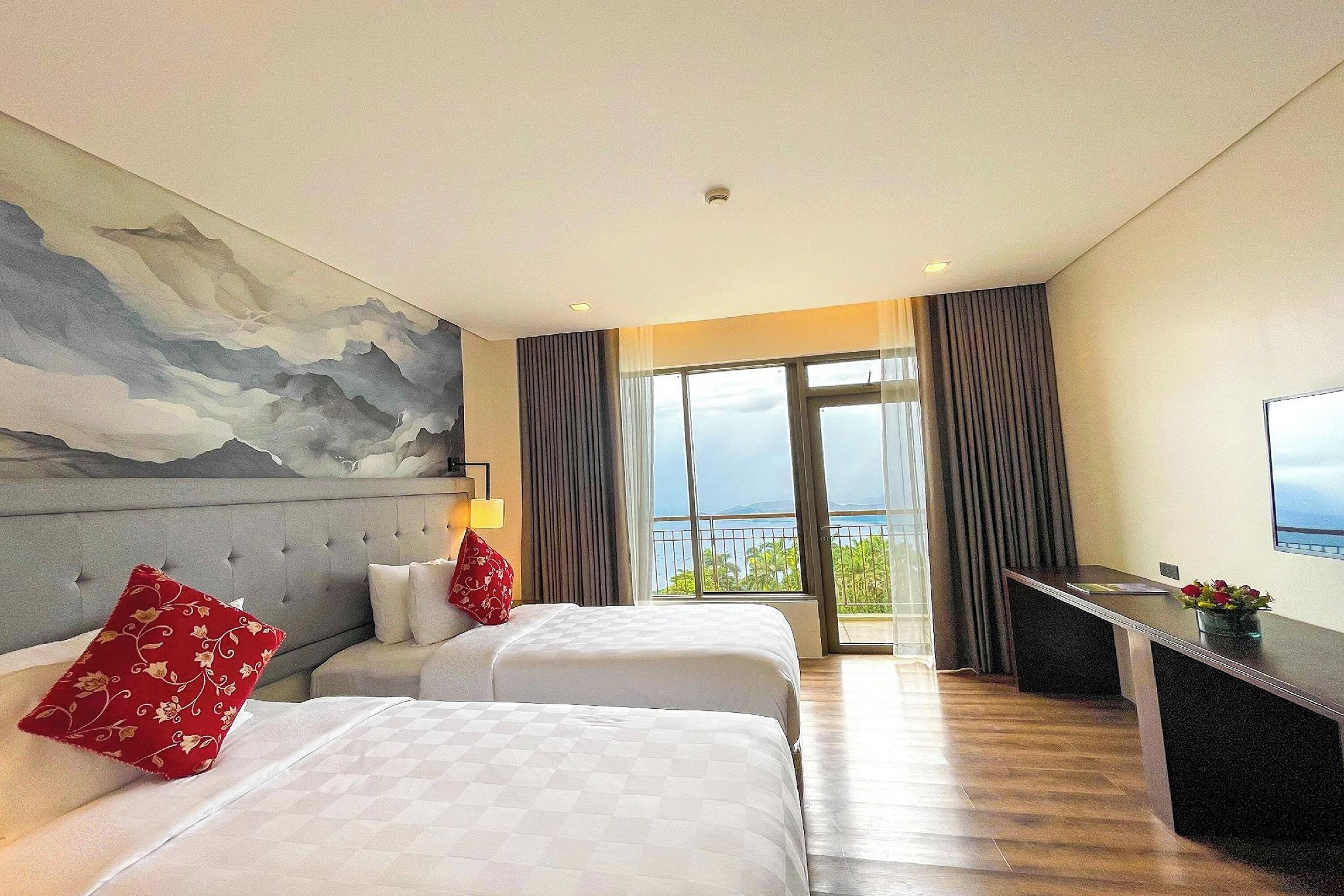 Habitación de hotel con dos camas, un cuadro grande en la pared, un escritorio con televisión y un balcón con vistas.