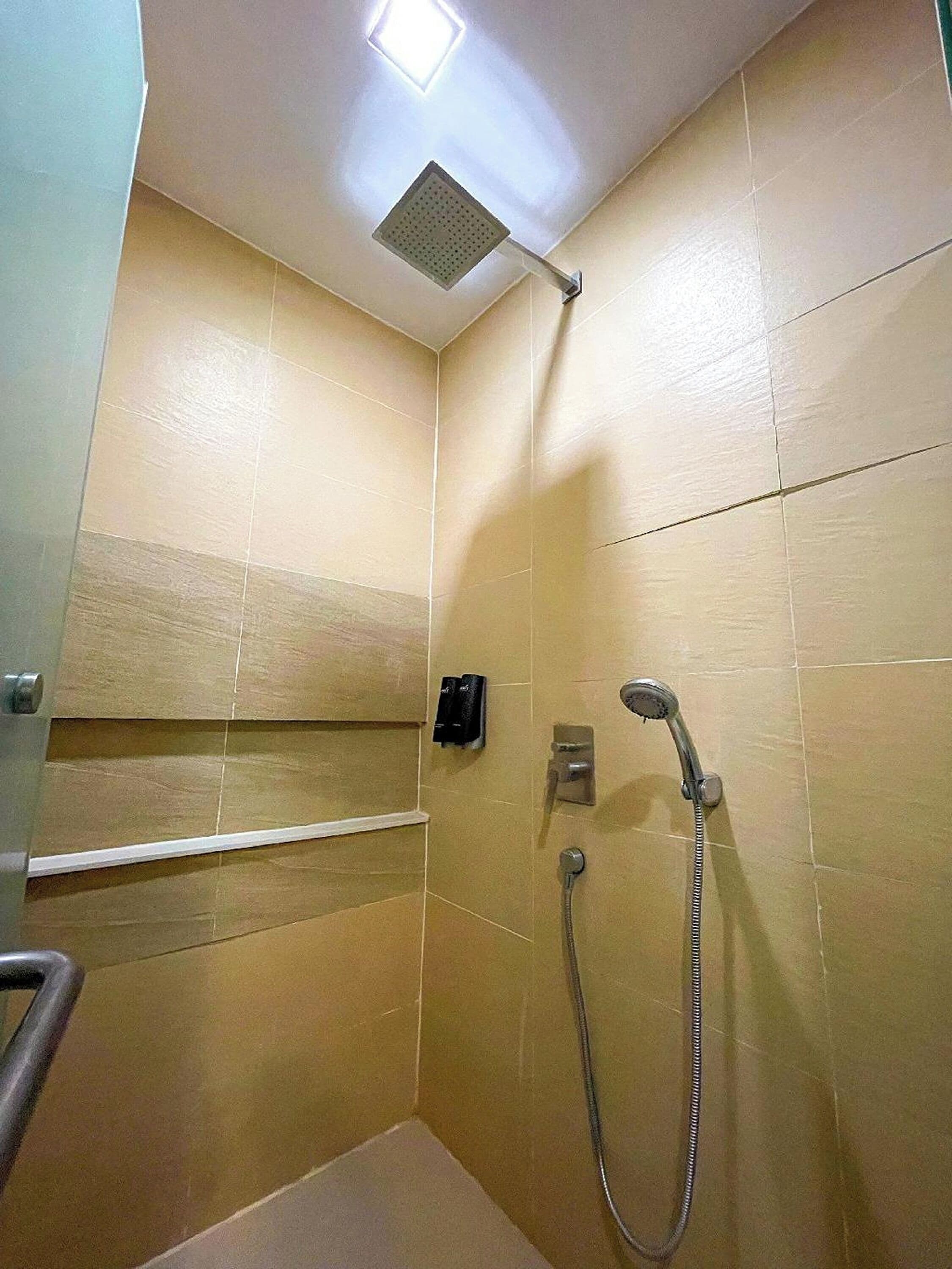 A small, tiled shower room with a handheld showerhead and a wall-mounted faucet.