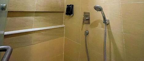 A small, tiled shower room with a handheld showerhead and a wall-mounted faucet.