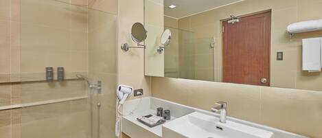 A modern bathroom with a glass shower enclosure, a large mirror, a white sink, and a wooden door.