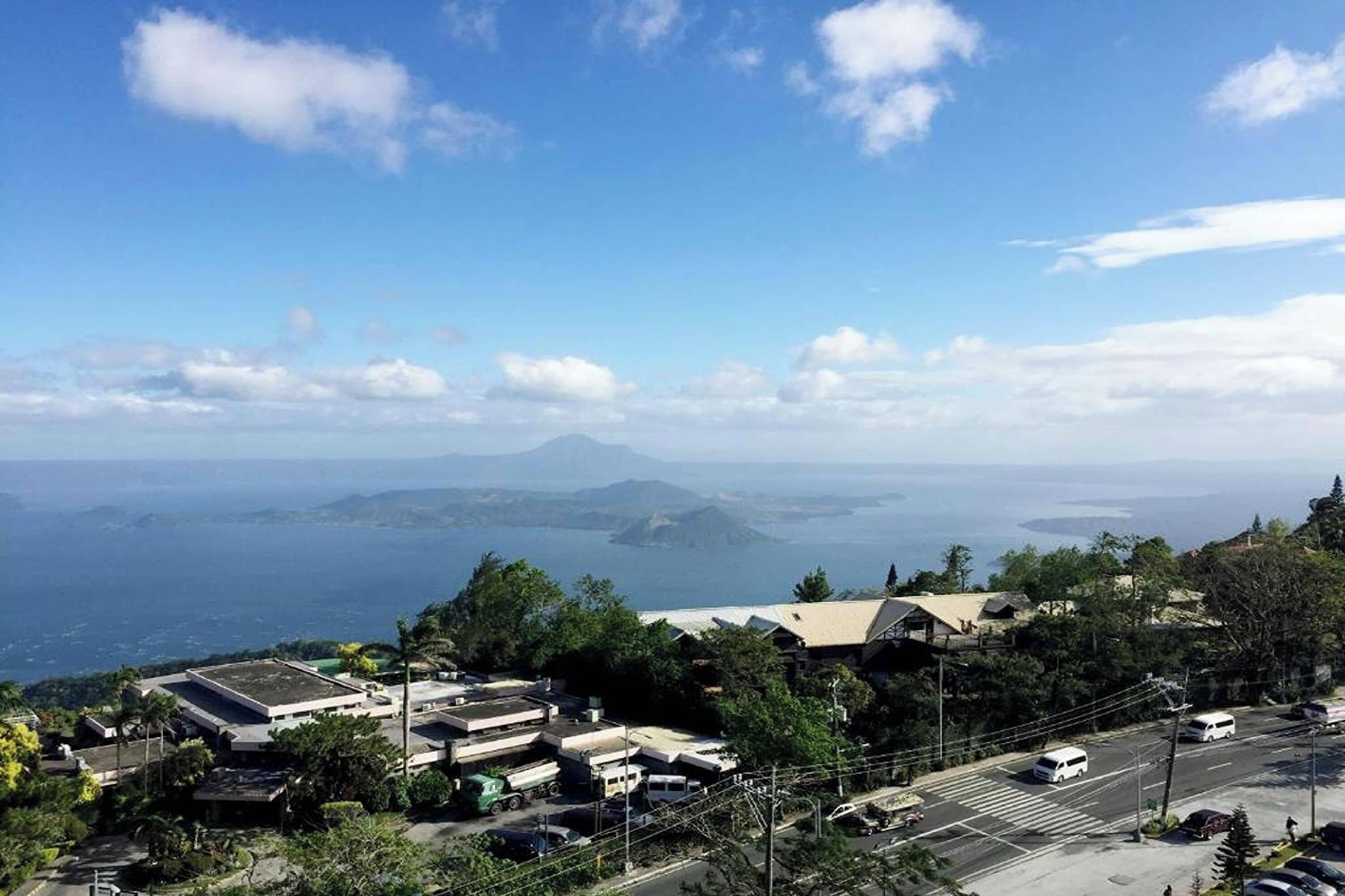 A coastal town with buildings, a road, and a view of the sea and mountains.