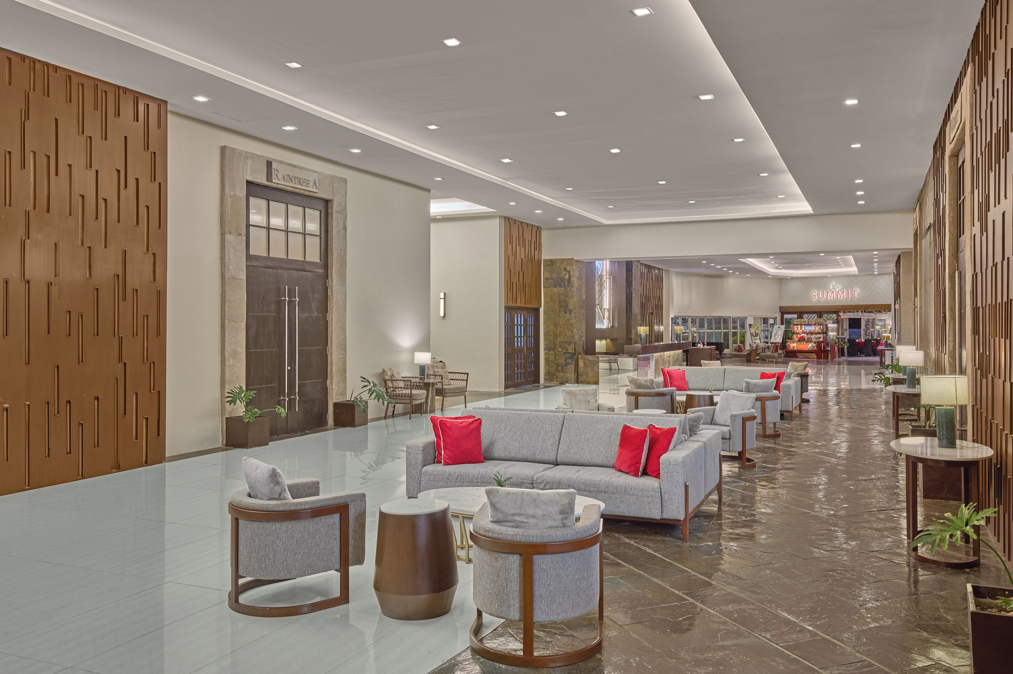 A spacious lobby with a grey sofa set, wooden panel walls, and a marble floor.