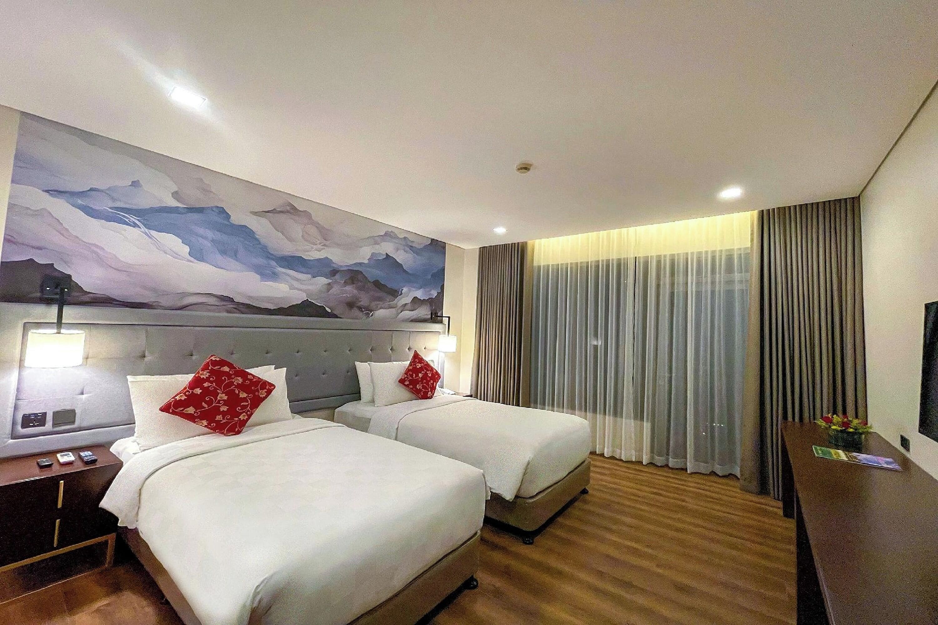 Une chambre d’hôtel avec deux lits, une grande peinture abstraite au mur, un bureau avec une lampe et un téléviseur sur le côté droit.