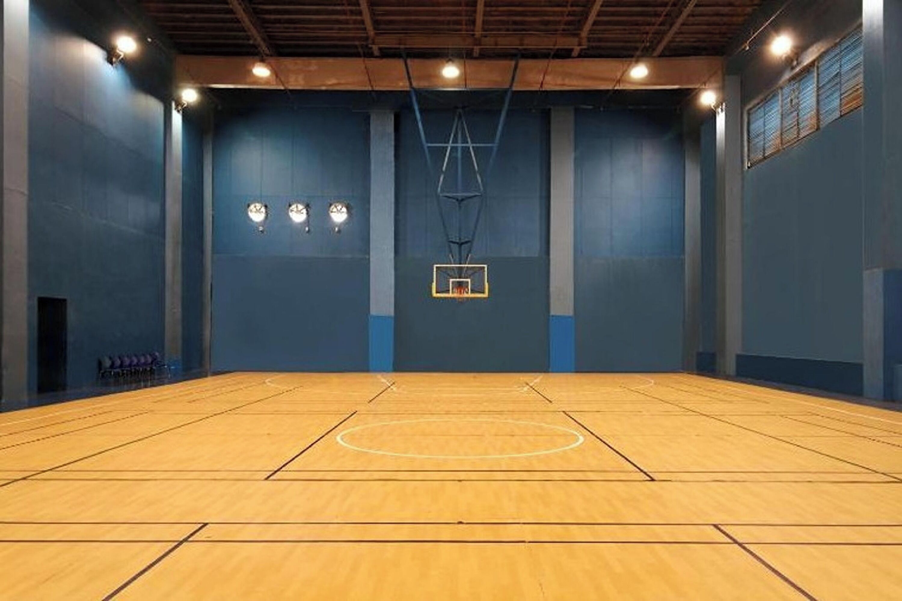 Una cancha de baloncesto cubierta con suelo de madera, aro de baloncesto y tres relojes en la pared.