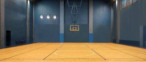 Una cancha de baloncesto cubierta con suelo de madera, aro de baloncesto y tres relojes en la pared.