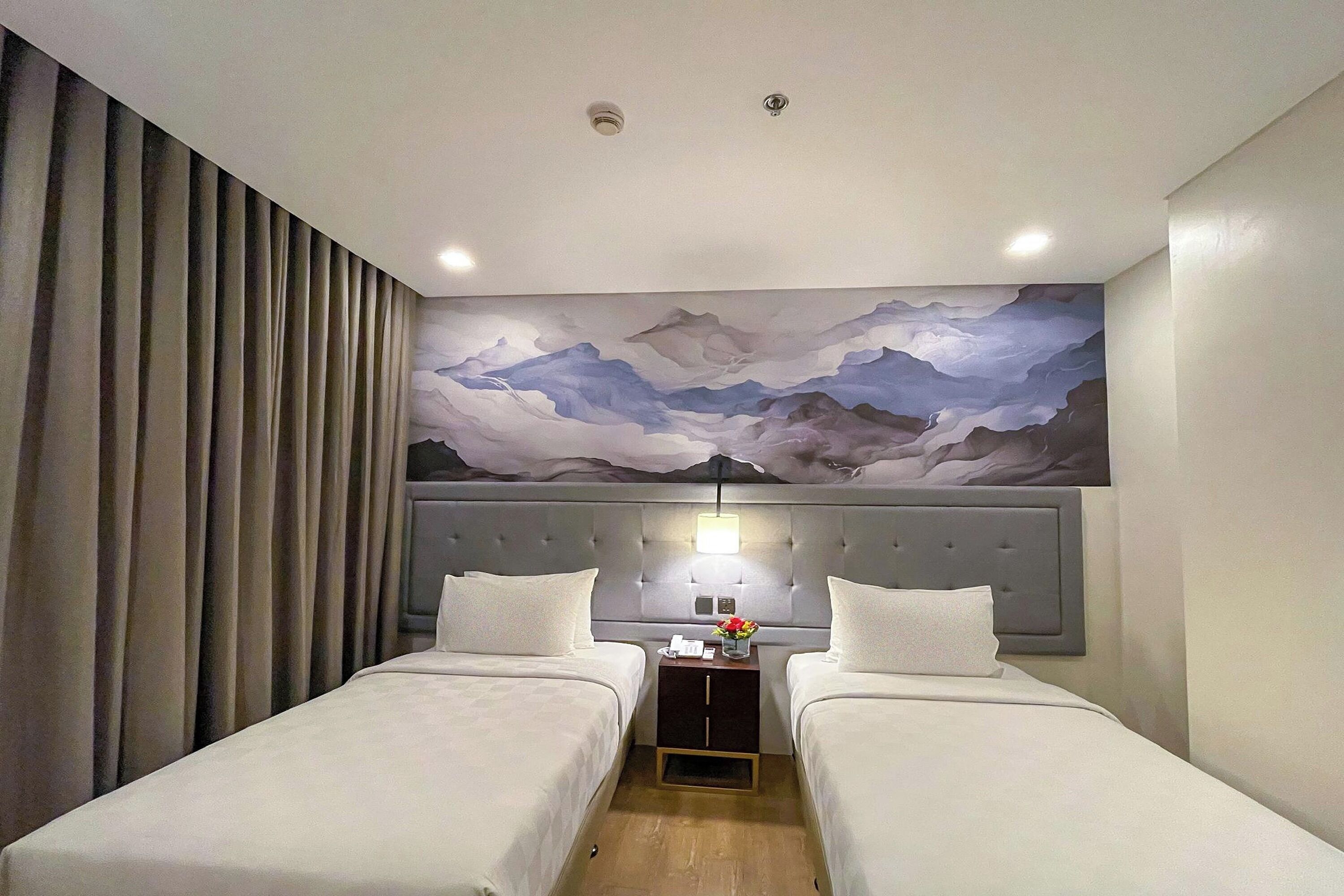 A hotel room with two beds, a nightstand with a lamp, and a large wall mural.