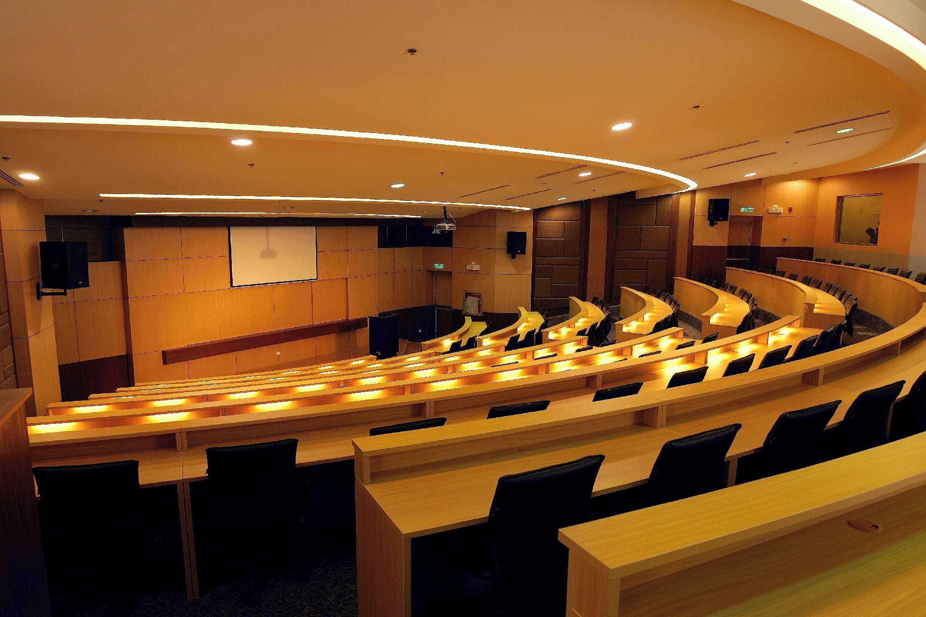 A modern conference room with tiered seating, a large screen, and built-in speakers.