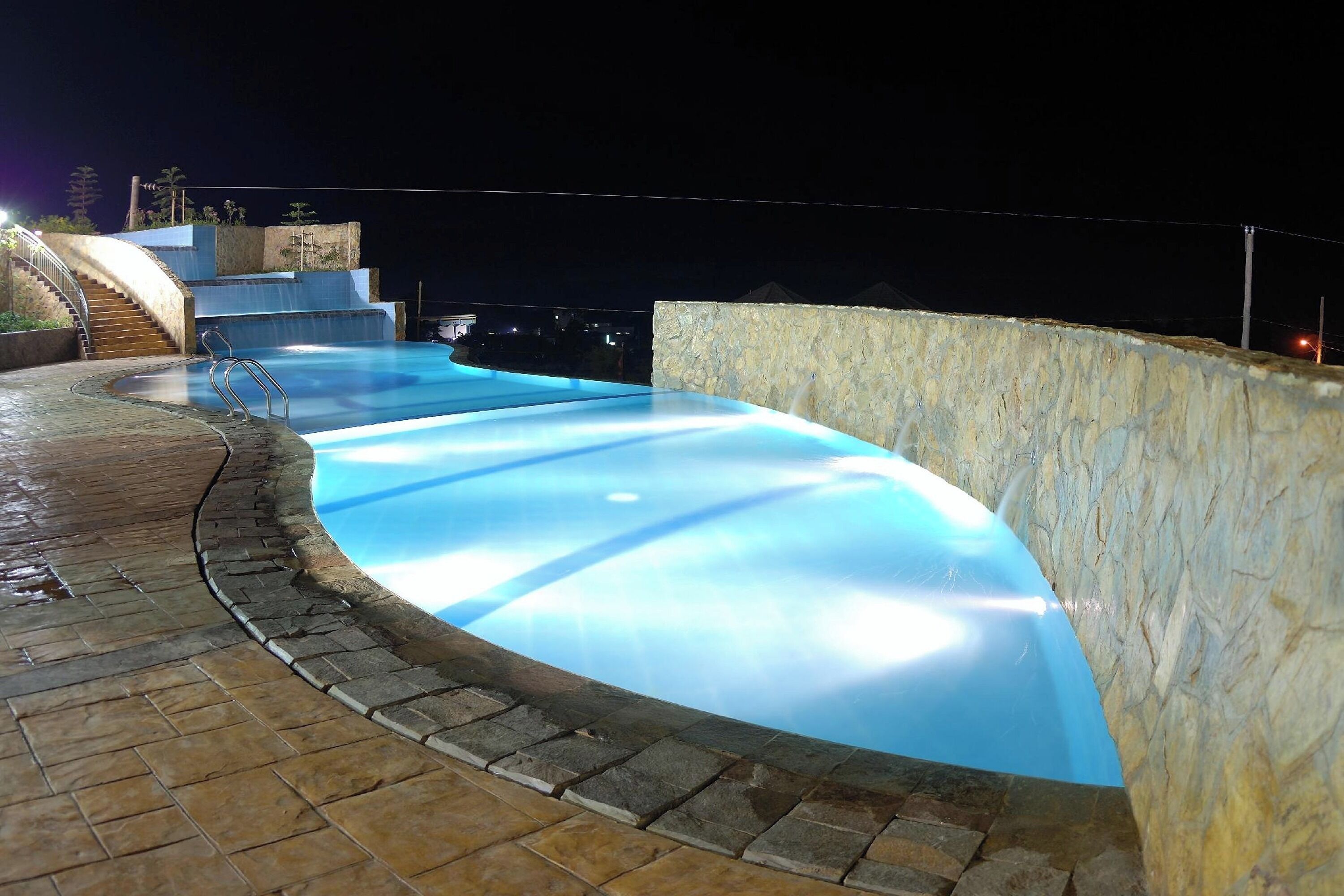 A swimming pool with a curved design, a stone wall, and a staircase leading to a higher level.