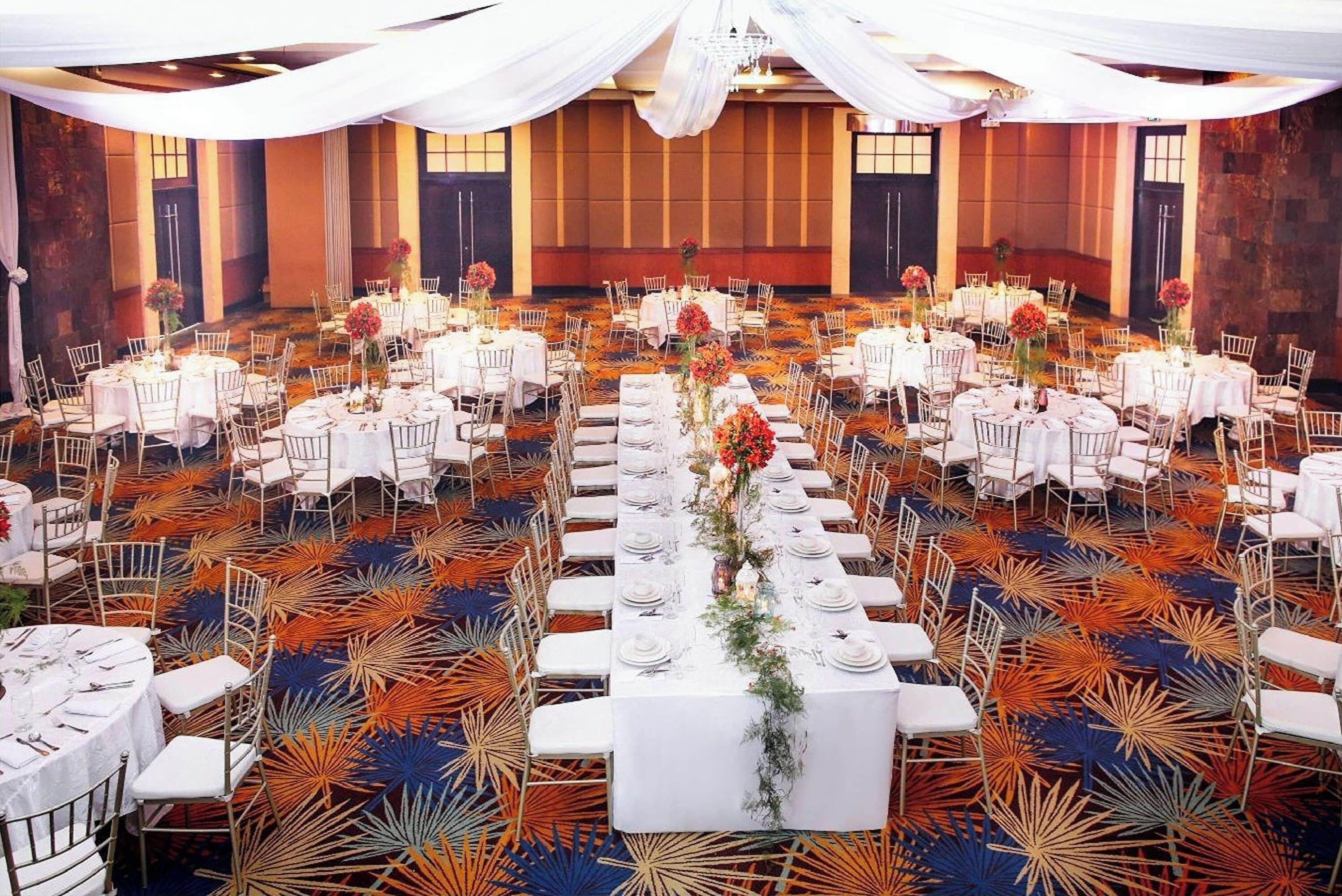 Un salón de banquetes con mesas redondas, manteles blancos y sillas.