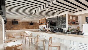 Un área de bar moderna con una barra blanca, sillas de madera y un menú en una pizarra.