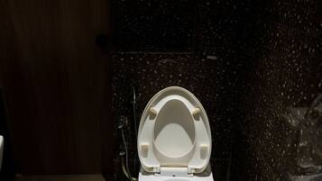 A toilet with a closed lid in a bathroom with a tiled floor and a dark speckled wall.