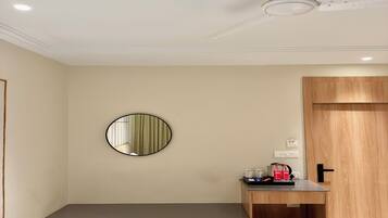 Una habitación moderna con un banco de madera, un espejo redondo, un ventilador de techo y una pequeña mesa de madera con una cafetera y botellas.