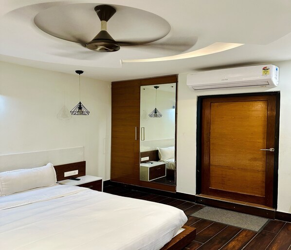 Habitación de hotel con cama, ventilador de techo, espejo, puerta de madera y unidad de aire acondicionado.