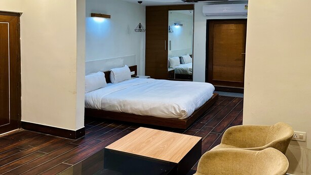 Ein Hotelzimmer mit einem Bett, einem Glastisch, zwei Sesseln, einem Deckenventilator und einem großen Spiegel.