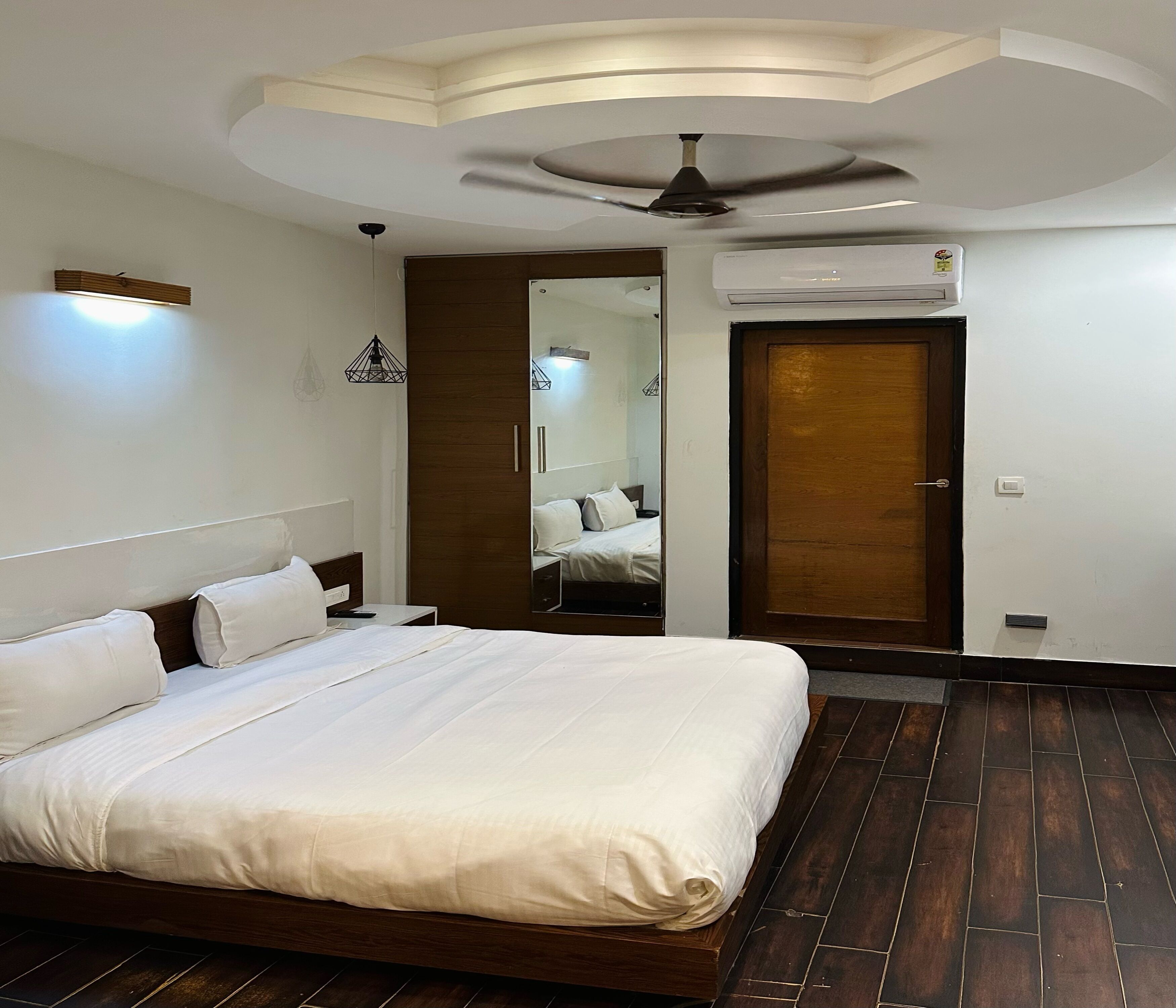 Un dormitorio con cama, ventilador de techo, armario, espejo y unidad de aire acondicionado.