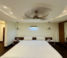 Habitación de hotel con una cama grande, dos mesitas de noche, un ventilador de techo y dos lámparas colgantes.