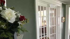Un pasillo con una puerta blanca, un jarrón con flores y un piso de madera oscura.
