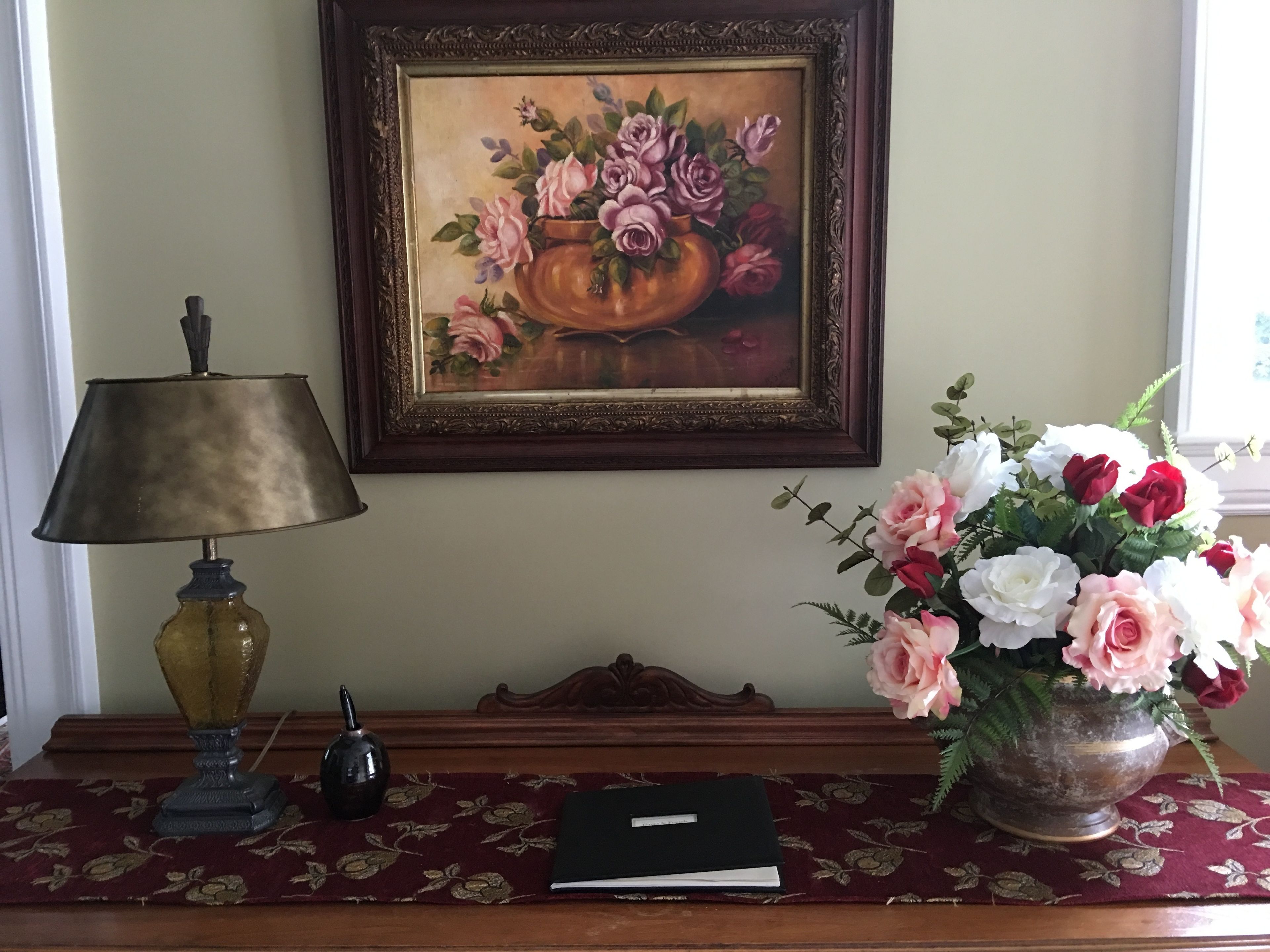 A desk with a lamp, a book, and a vase of flowers.