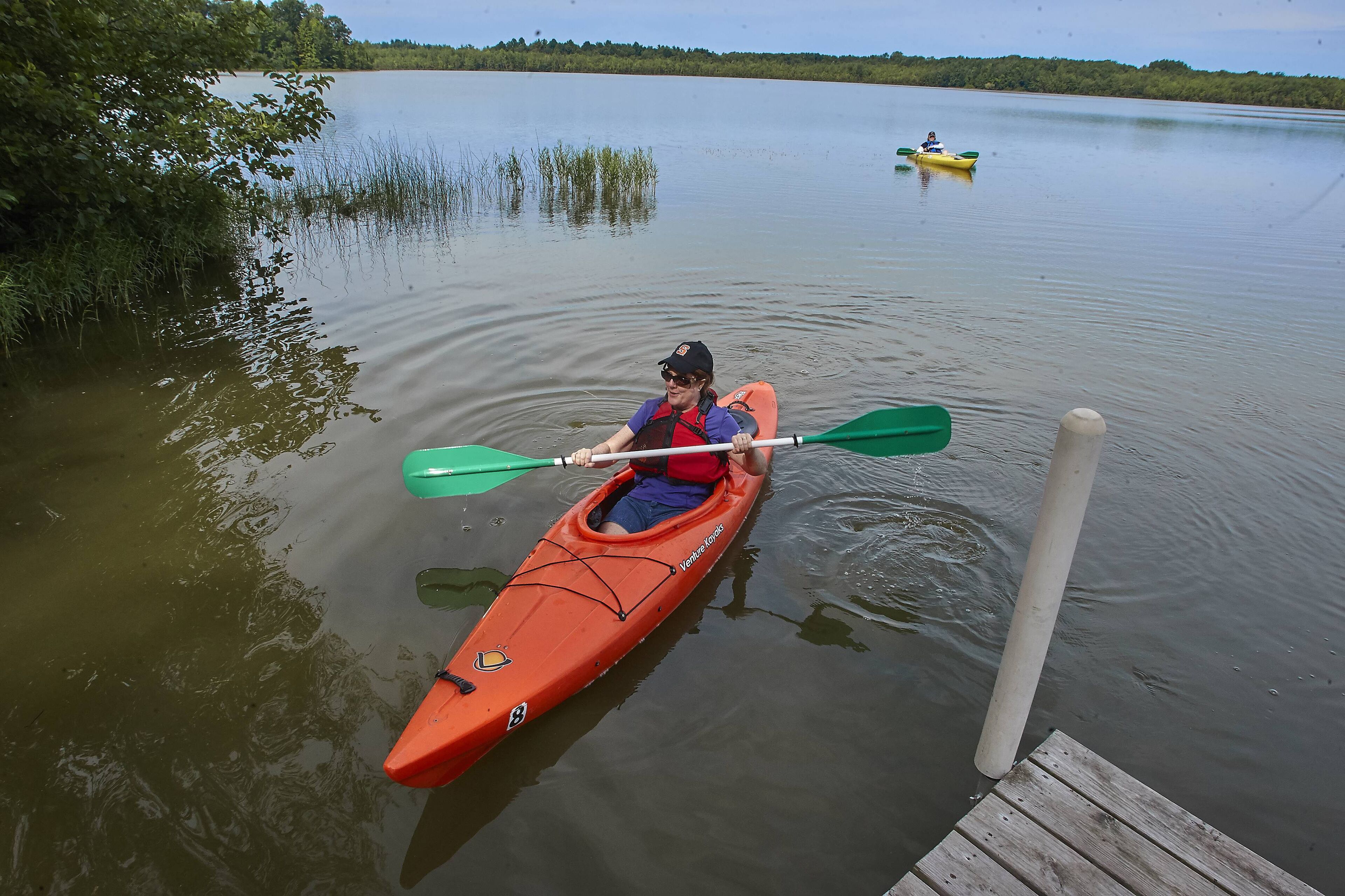 A person in a kayak on calm water near a dock.