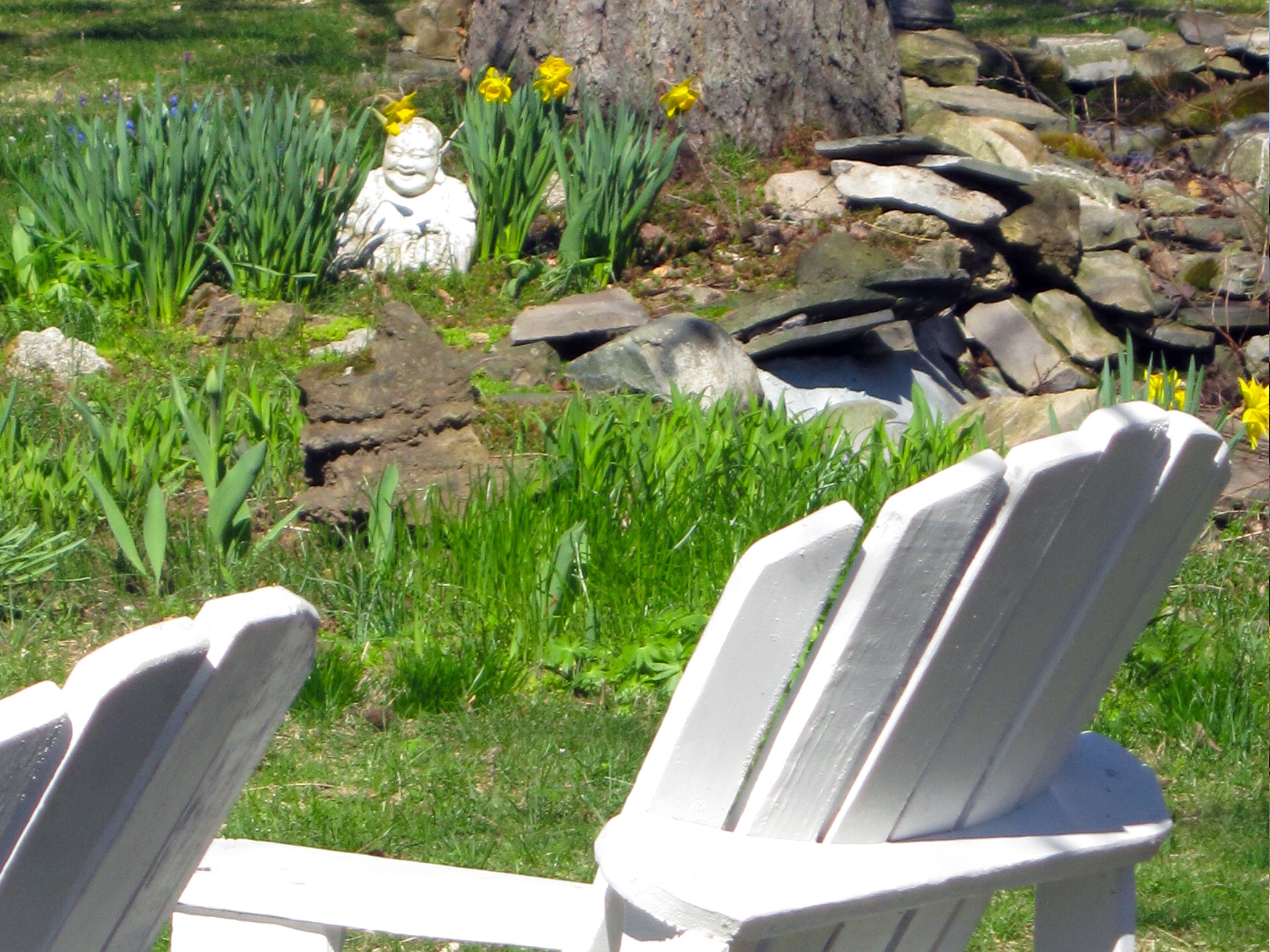 A garden with a statue, yellow flowers, and a white chair.