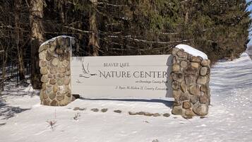 A stone sign for Beaver Lake Nature Center with a bird illustration, surrounded by snow and trees.