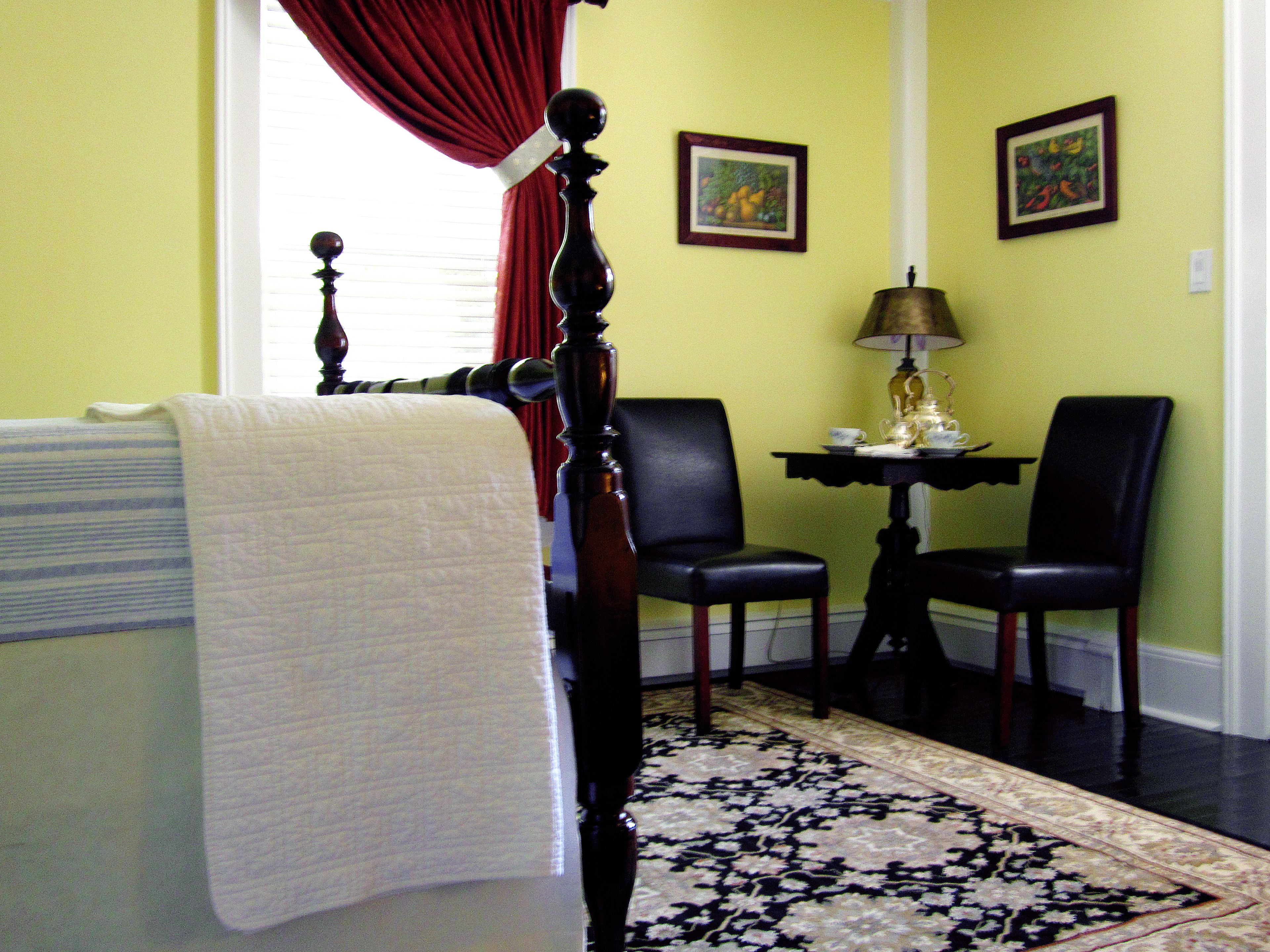 A room with a bed, a chair, a table with a lamp, and two framed pictures on the wall.