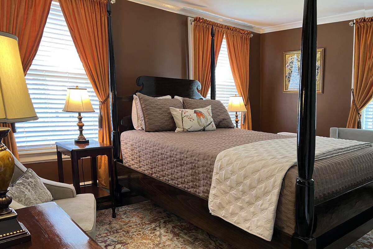 A four-poster bed with a quilted headboard, two bedside lamps, and a patterned rug.