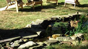 Un jardín con un estanque, rodeado de sillas Adirondack de madera.